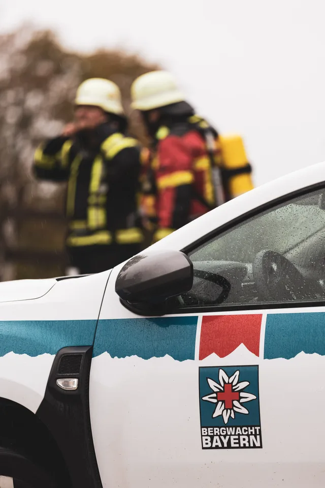 Zwei Teilnehmer mit weißen Helmen hinter einem Rettungsfahrzeug.