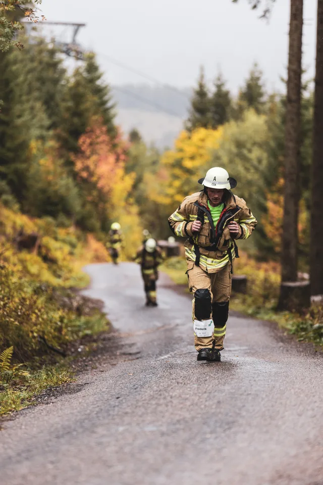 Teilnehmer mit weißem Helm und beiger Einsatzkleidung auf der nassen Bergstraße.