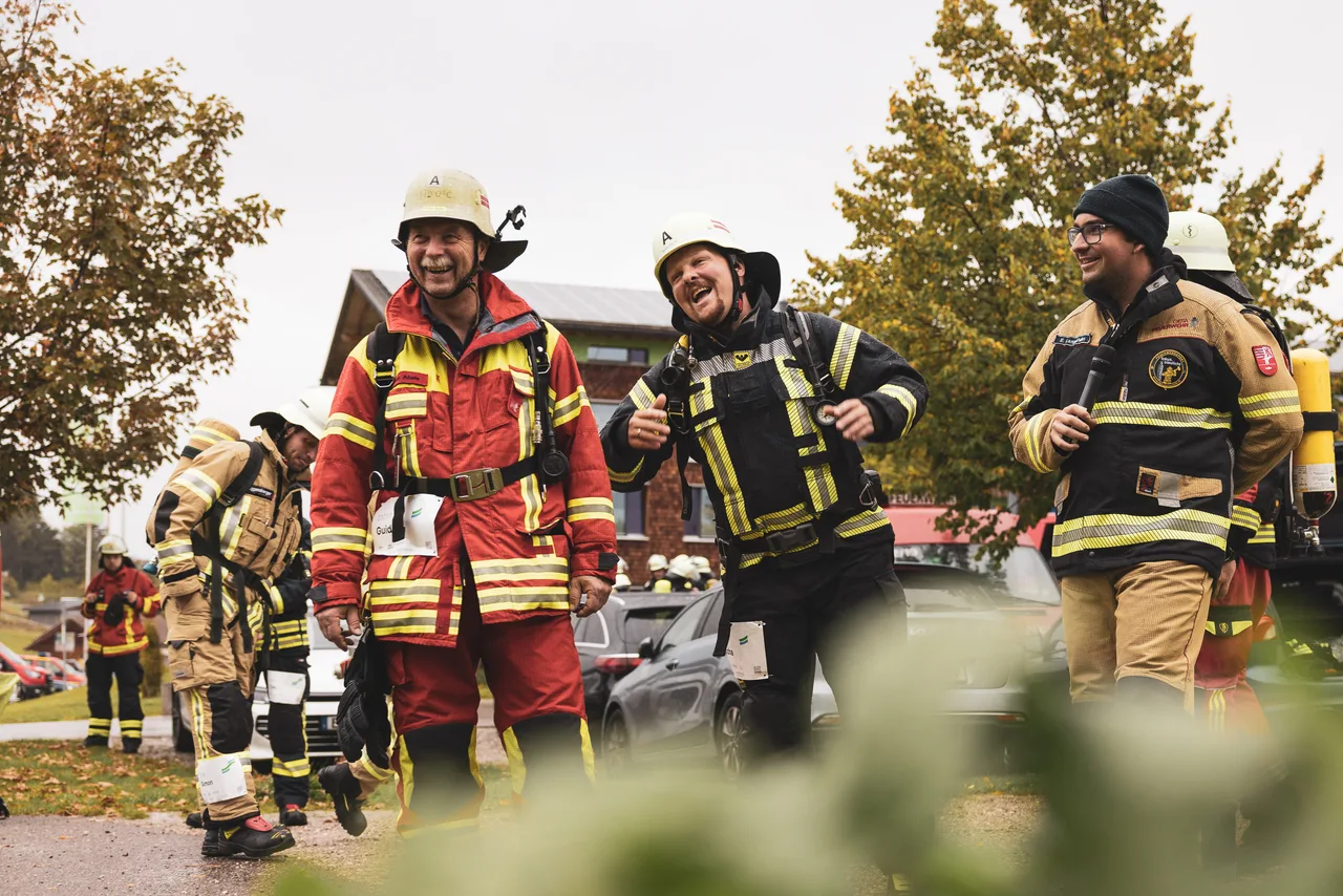 Lachende Feuerwehrleute mit geschulterten Atemschutzgeräten warten im herbstlichen Startbereich.