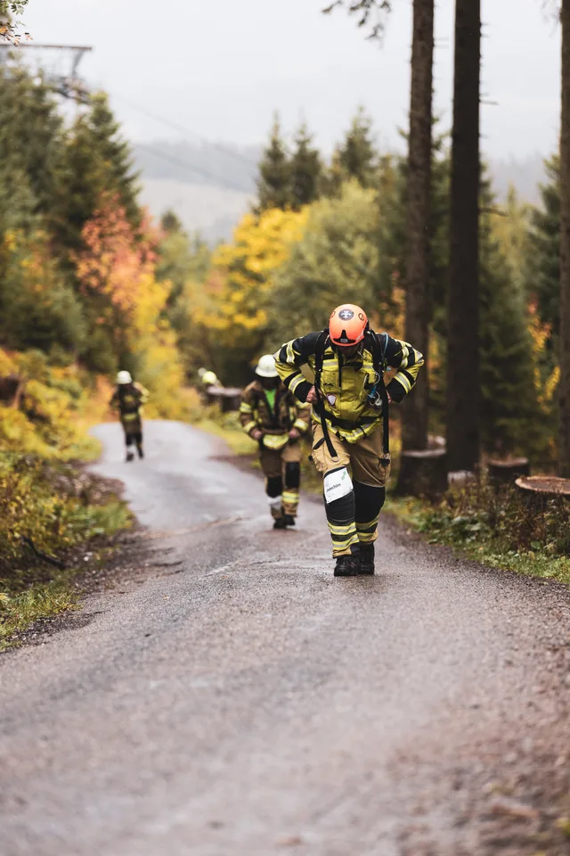 Teilnehmer mit orangefarbenem Helm steigt vor weiteren Läufern die Bergstraße hinauf.