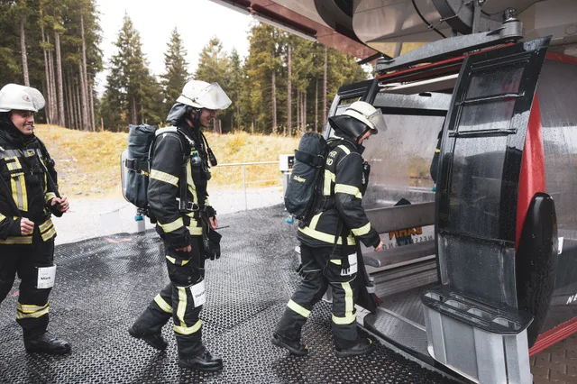 Teilnehmer mit Atemschutzgeräten steigen an der Bergstation in die Gondel.
