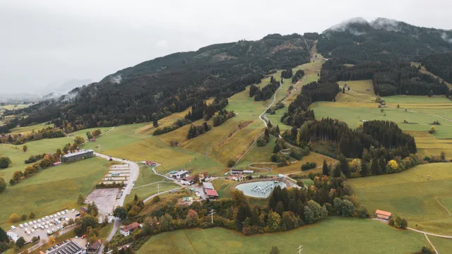 Luftaufnahme des Berghangs und der Talstation unter tiefen Wolken.