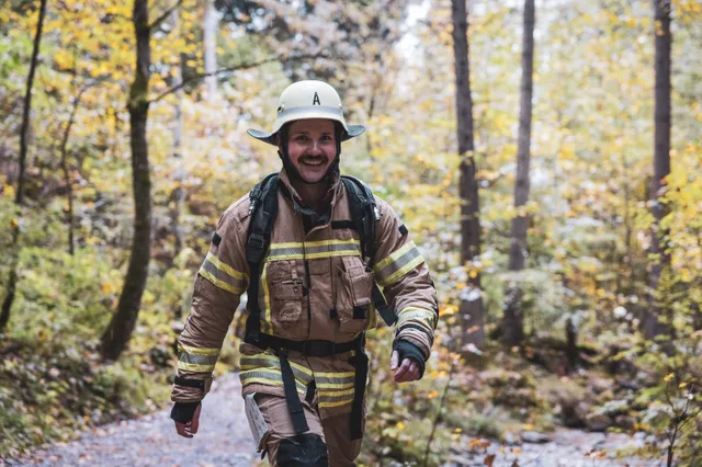 Lächelnder Teilnehmer in beiger Einsatzkleidung und hellem Helm im Wald.