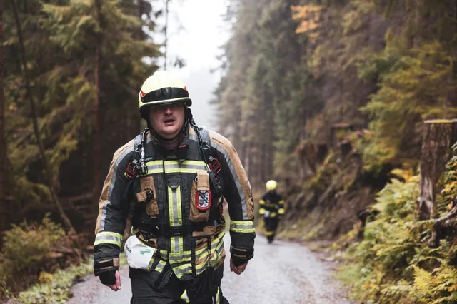 Teilnehmer in dunkler Einsatzkleidung und hellem Helm auf der Bergstraße im Wald.