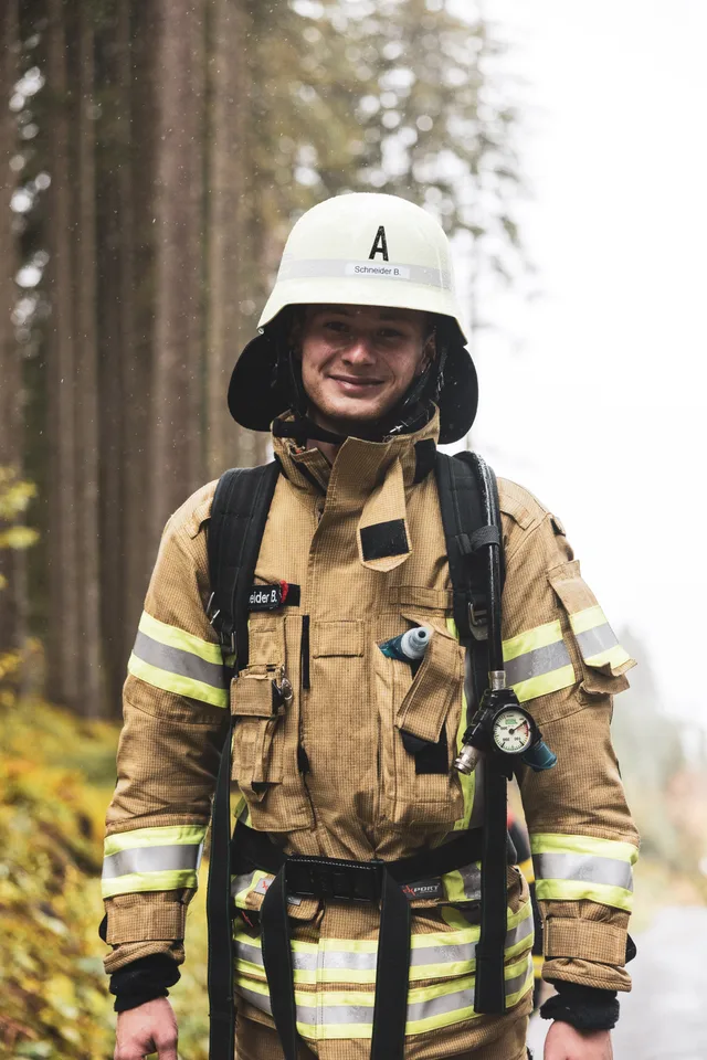 Lächelnder Teilnehmer in beiger Einsatzkleidung und weißem Helm auf der Bergstraße.
