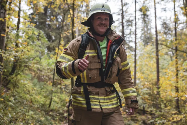 Lächelnder Teilnehmer in beiger Einsatzkleidung und hellem Helm im Wald.