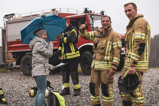 Teilnehmer und Zuschauer mit Regenschirmen vor einem Feuerwehrfahrzeug.