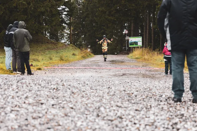 Teilnehmer in schwarzer Einsatzkleidung läuft über den nassen Schotter ins Ziel.
