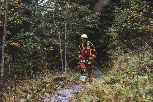 Teilnehmer in roter Einsatzkleidung auf einem schmalen Waldweg.