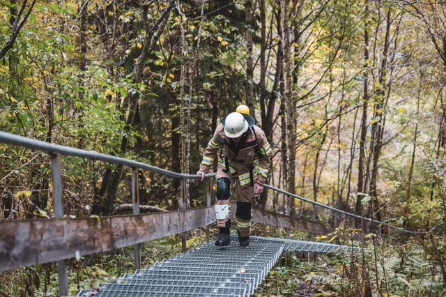 Teilnehmer in beiger Einsatzkleidung auf einer Metalltreppe zwischen Bäumen.