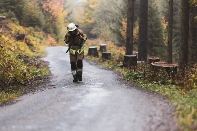 Teilnehmer in beiger Einsatzkleidung steigt vornübergebeugt die nasse Bergstraße hinauf.