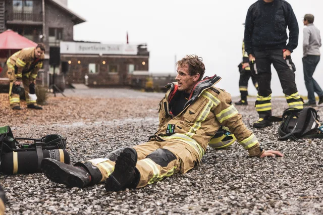 Feuerwehrmann sitzt mit ausgestreckten Beinen auf nassem Schotter vor dem Sportheim Böck.