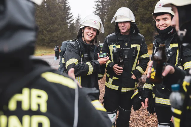 Lachende Teilnehmer mit hellen Helmen und Getränken nach dem Lauf.