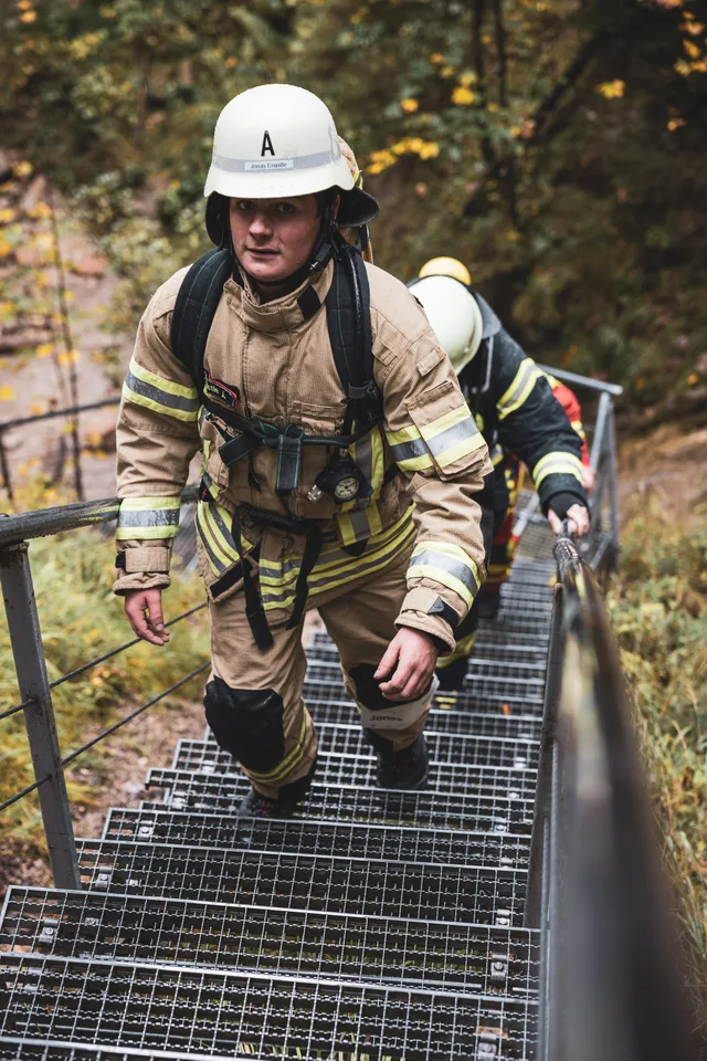 Lächelnder Teilnehmer in beiger Einsatzkleidung auf den Metallstufen.