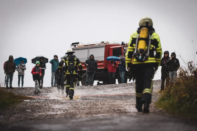 Feuerwehrleute laufen durch Pfützen zur Zielmarkierung vor Zuschauern mit Regenschirmen.