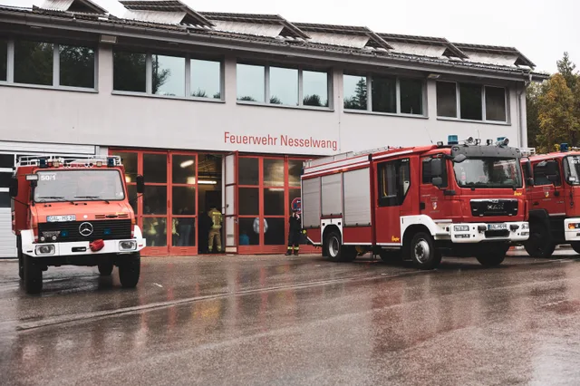Feuerwehrfahrzeuge vor dem Feuerwehrhaus Nesselwang auf nassem Vorplatz.