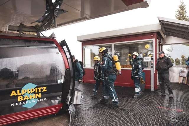 Teilnehmer in Einsatzkleidung steigen an der Bergstation in eine rote Gondel.