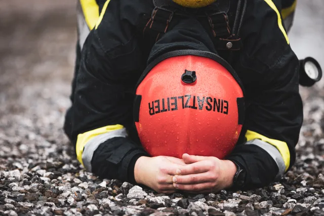 Teilnehmer mit rotem Helm stützt den Kopf auf den Unterarmen auf dem Schotter ab.