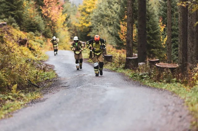 Teilnehmer mit orangefarbenem Helm steigt vor weiteren Läufern die Bergstraße hinauf.