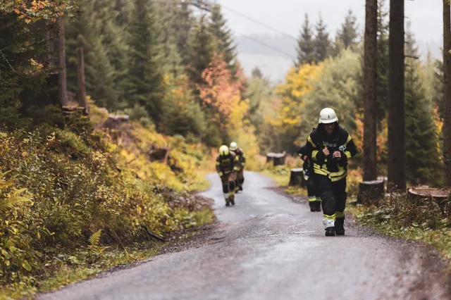 Teilnehmer in dunkler Einsatzkleidung steigt vor weiteren Läufern die nasse Bergstraße hinauf.