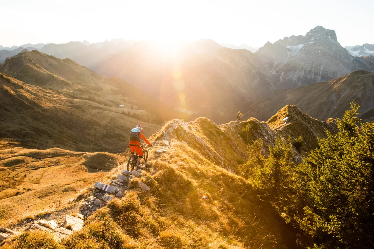Mountainbiker fährt auf einem steinigen Gratweg durch goldenes Licht über dem Kleinwalsertal