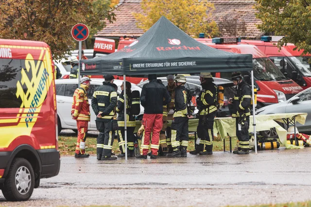 Teilnehmer unter einem Zelt neben Feuerwehrfahrzeugen.