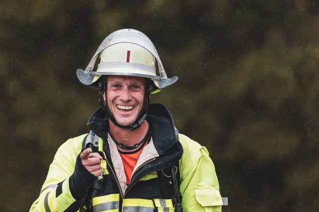 Lachender Teilnehmer mit weißem Helm zeigt im Regen in die Kamera.