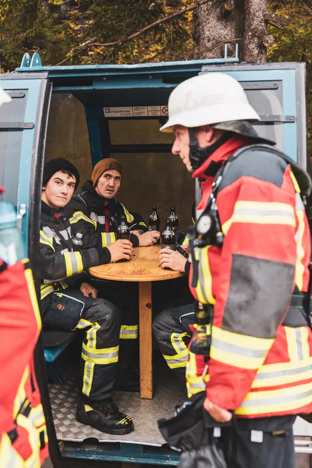 Teilnehmer in roter Einsatzkleidung vor einer als Sitzplatz genutzten Gondel.