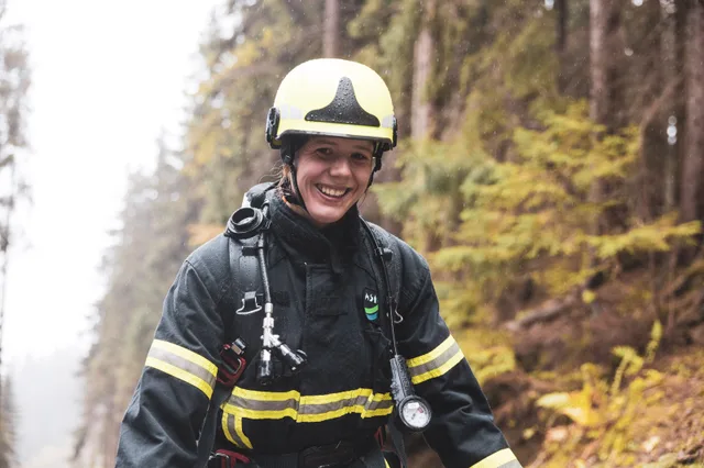 Lachende Teilnehmerin mit gelbem Helm und schwarzer Einsatzkleidung beim Aufstieg.