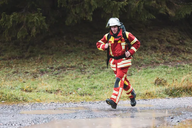 Teilnehmer in roter Einsatzkleidung läuft über den nassen Schotter ins Ziel.