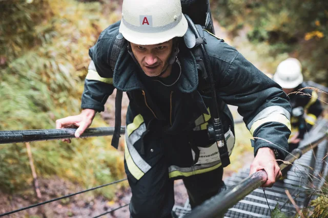 Teilnehmer in schwarzer Einsatzkleidung und weißem Helm steigt die Waldtreppe hinauf.