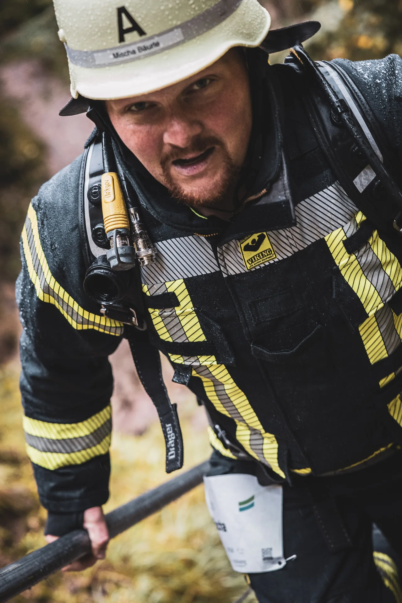 Feuerwehrmann mit regennassem Helm und Atemschutzgerät greift beim Aufstieg an ein Geländer.