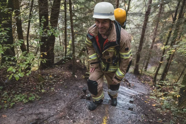 Teilnehmer mit weißem Helm und Atemschutzgerät auf steilen Waldstufen.