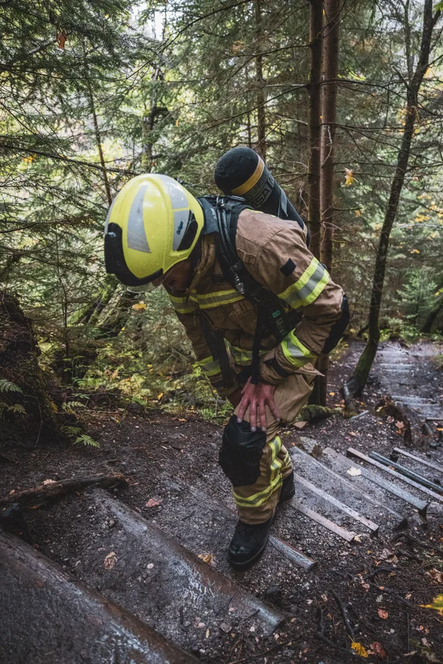 Teilnehmer in beiger Einsatzkleidung und gelbem Helm auf steilen Waldstufen.