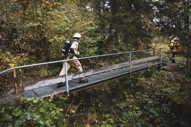 Teilnehmer mit Atemschutzgerät auf einer schmalen Metallbrücke.