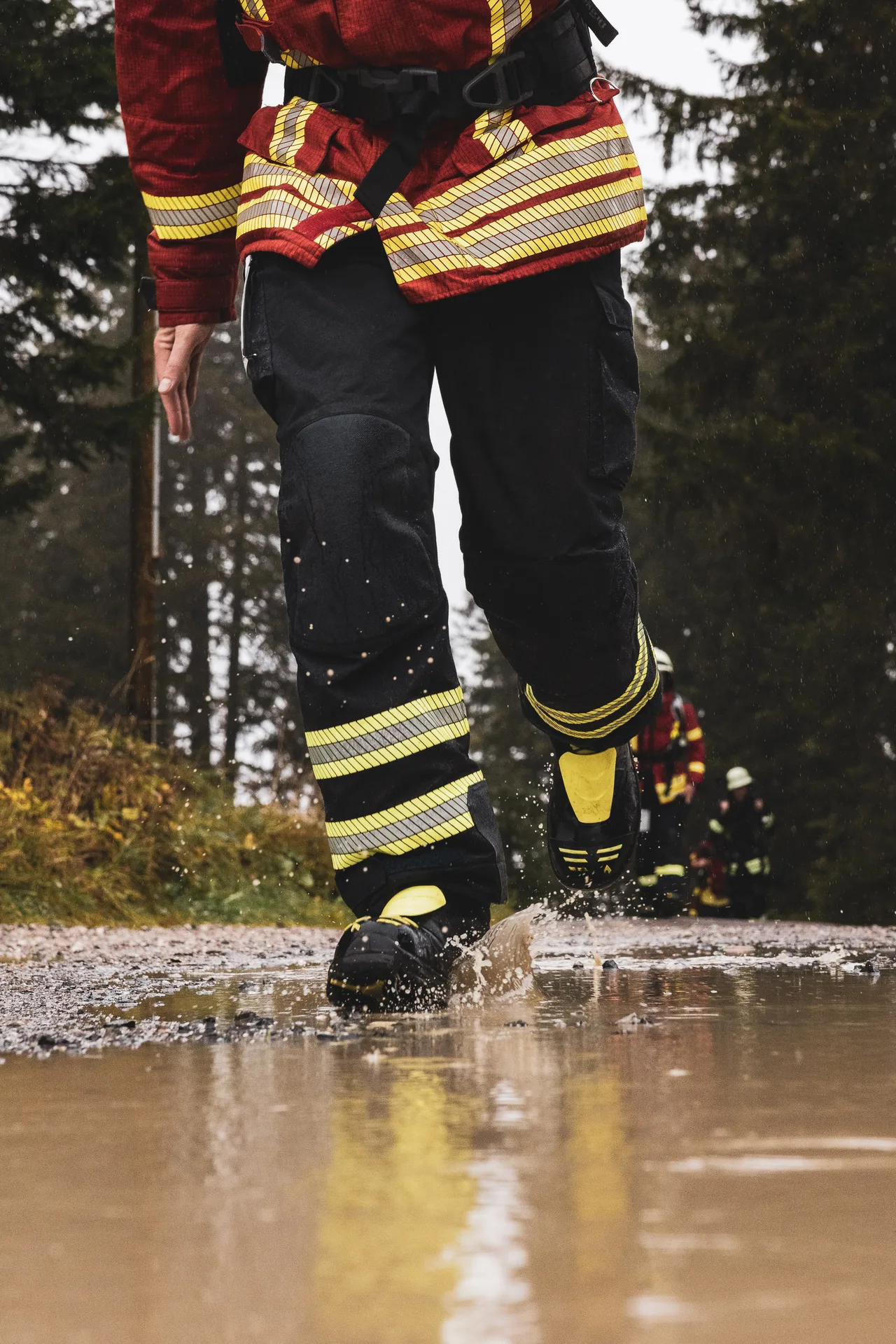 Einsatzstiefel eines Teilnehmers spritzen beim Laufen durch eine Pfütze Wasser auf.