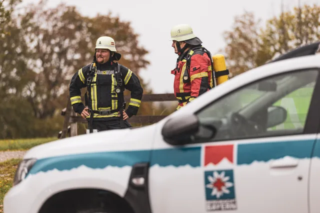Zwei Teilnehmer mit weißen Helmen hinter einem Rettungsfahrzeug.