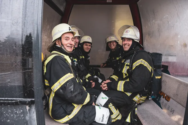 Lachende Gruppe in Einsatzkleidung sitzt in einer Gondel.