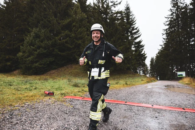 Teilnehmer in schwarzer Einsatzkleidung überquert die rote Zielmarkierung.