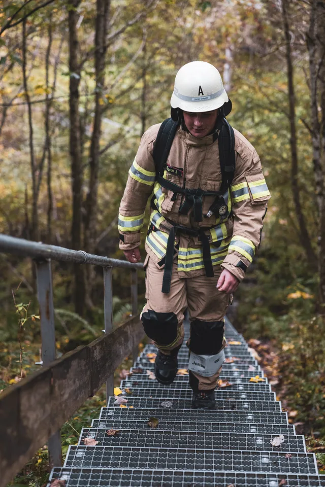 Teilnehmer mit weißem Helm und beiger Einsatzkleidung steigt eine lange Metalltreppe hinauf.
