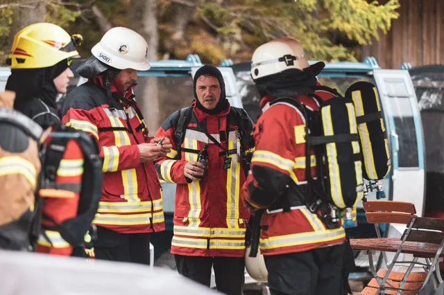 Teilnehmer in roter Einsatzkleidung unter einem Schirm im Gespräch.
