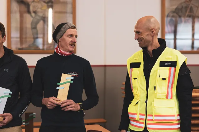 Teilnehmer mit grauer Mütze hält einen Pokal neben dem Organisator.