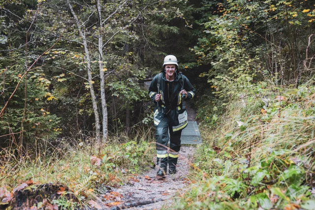 Lächelnder Teilnehmer mit grauem Helm und schwarzer Einsatzkleidung auf dem Waldweg.