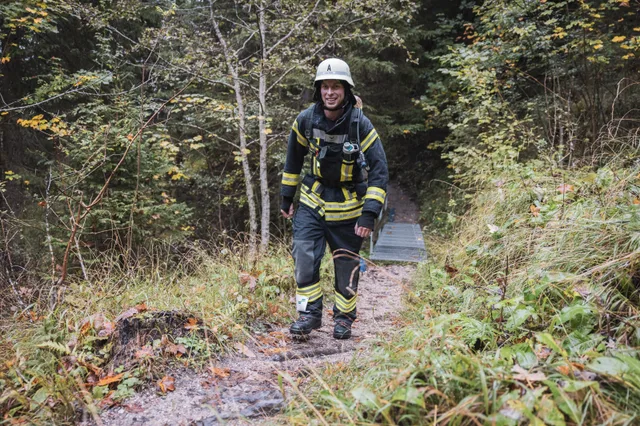 Lächelnder Teilnehmer mit grauem Helm und schwarzer Einsatzkleidung auf dem Waldweg.