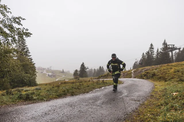 Teilnehmer in schwarzer Einsatzkleidung steigt über dem nebligen Tal bergauf.