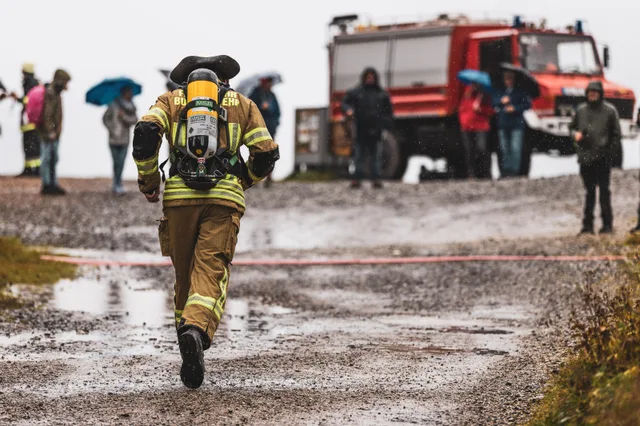 Feuerwehrteilnehmer läuft im Regen auf eine rote Bodenmarkierung und wartende Zuschauer zu.