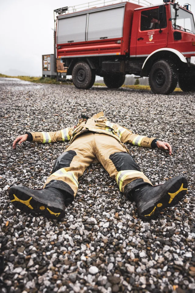 Teilnehmer liegt mit ausgestreckten Armen auf dem Schotter vor einem Feuerwehrfahrzeug.