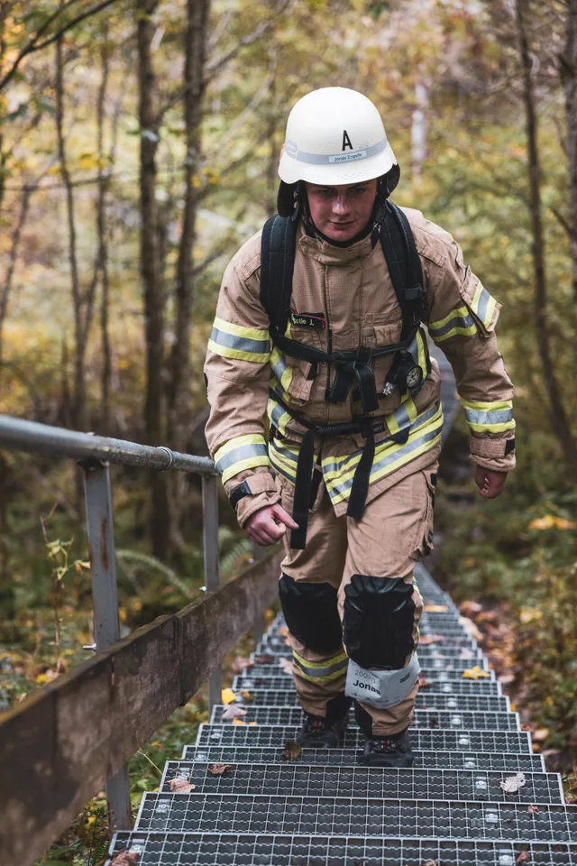 Teilnehmer mit weißem Helm und beiger Einsatzkleidung steigt eine lange Metalltreppe hinauf.