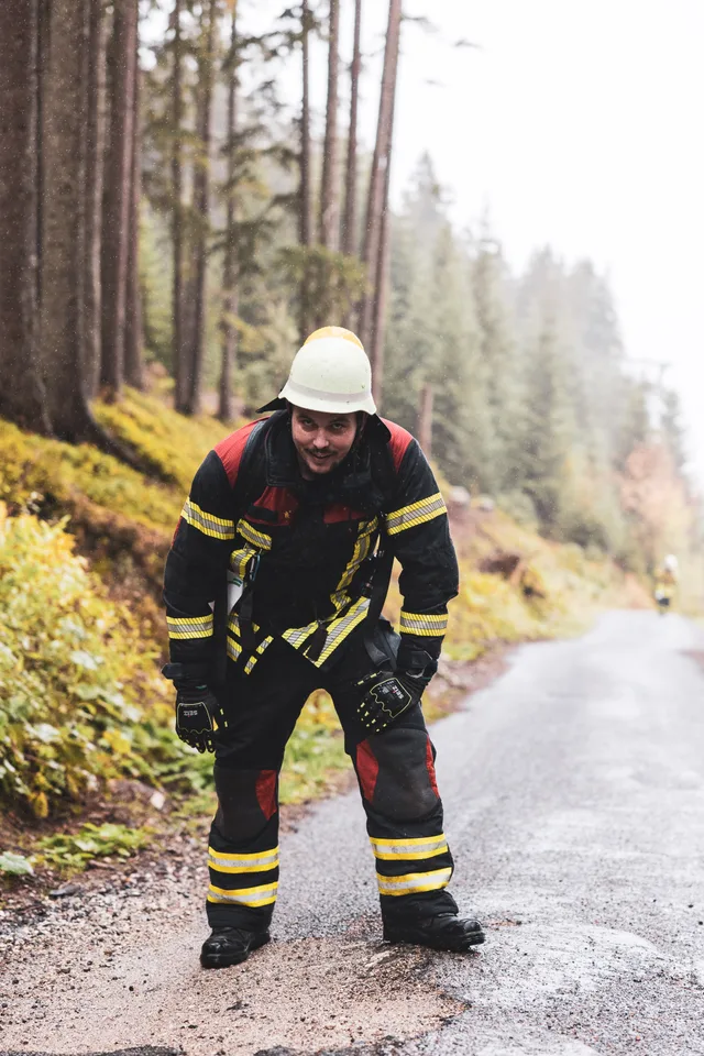 Teilnehmer mit weißem Helm beugt sich auf der nassen Bergstraße nach vorn.