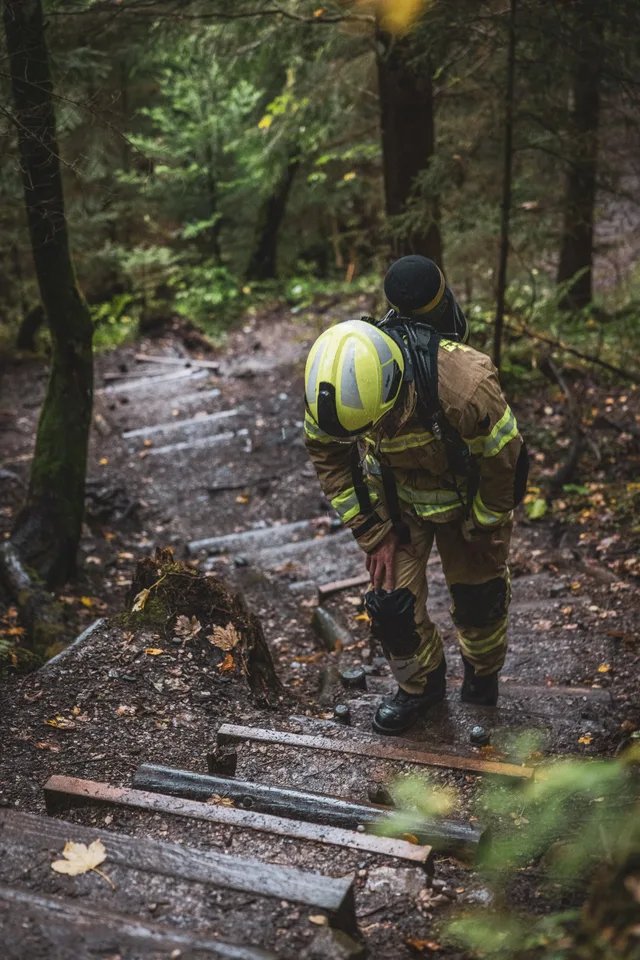 Teilnehmer in beiger Einsatzkleidung und gelbem Helm auf steilen Waldstufen.